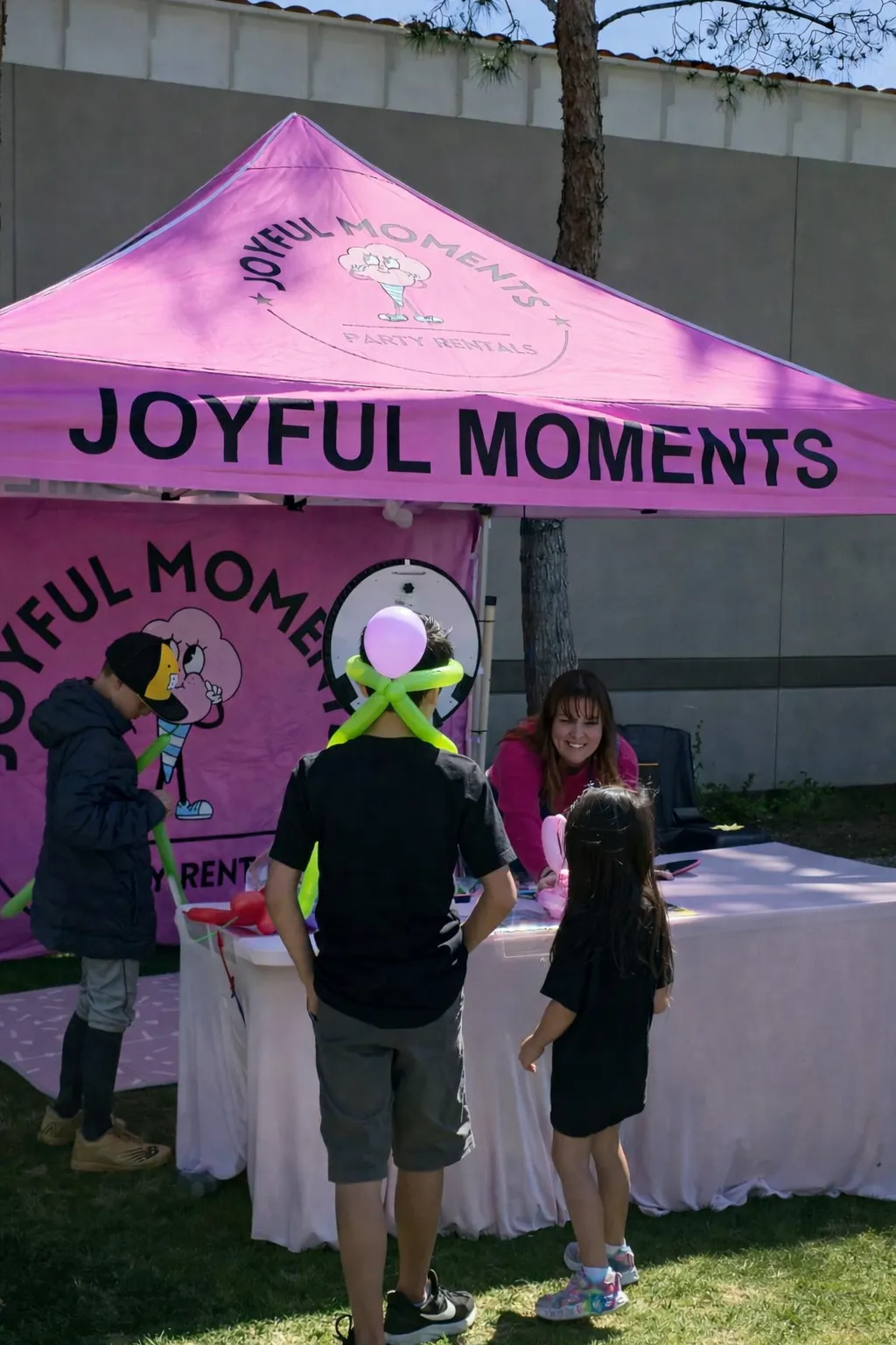 Children receiving balloon animals at the Joyful Moments Party Rentals booth