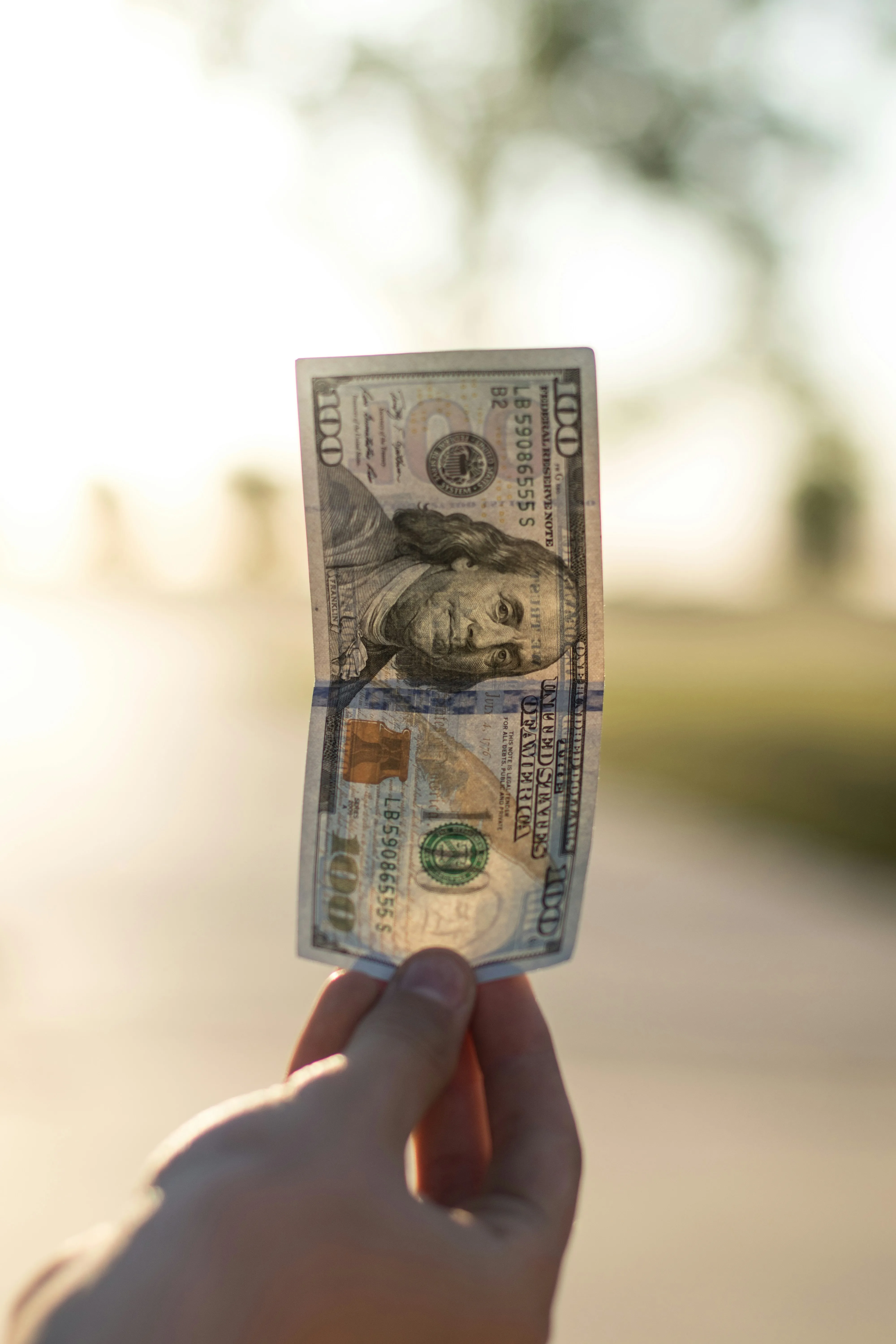 An image of a man holding a $100 bill in the sun.