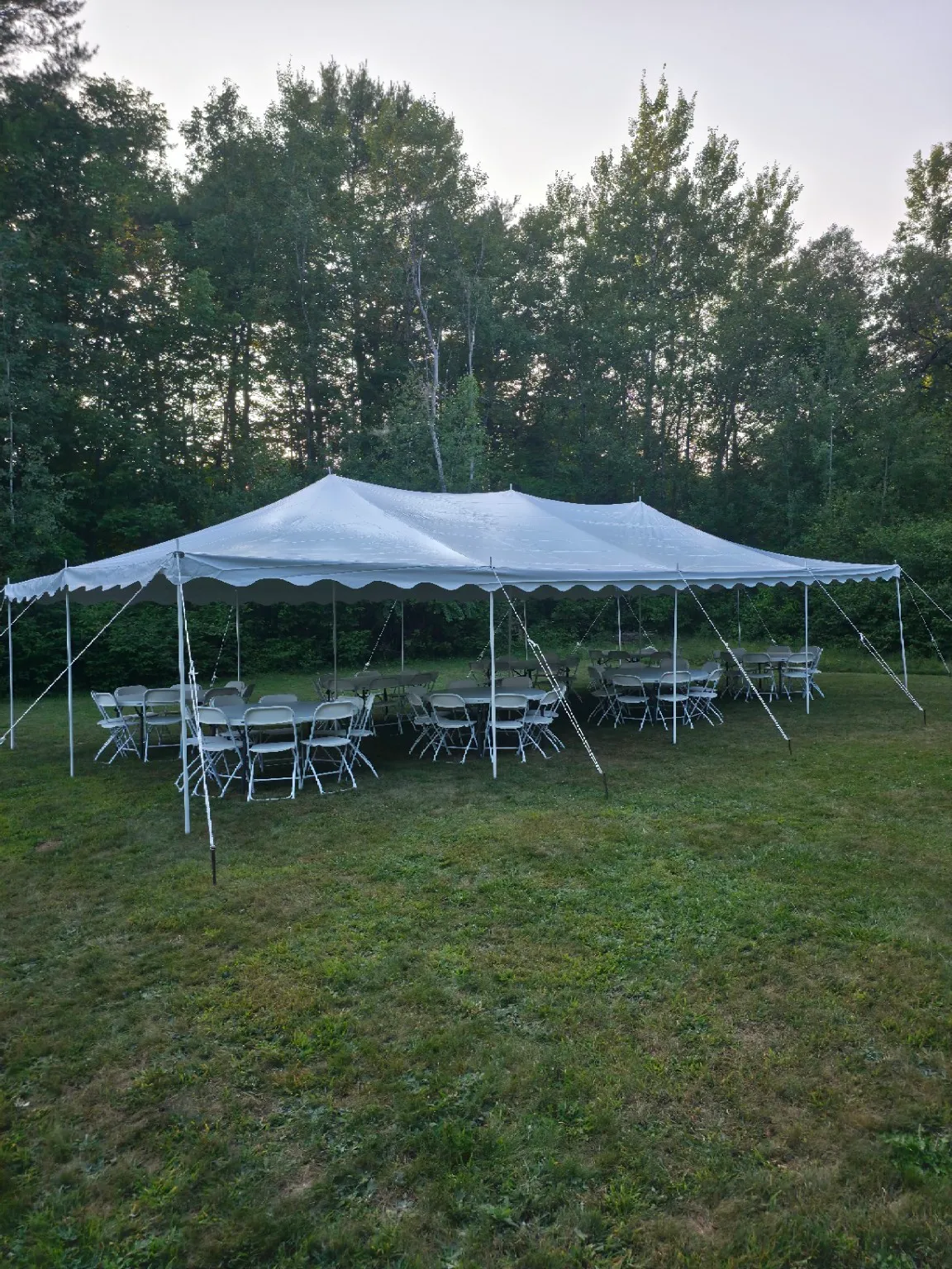 A 20x40 pole tent setup in the backyard with round tables and premium plastic folding chairs.