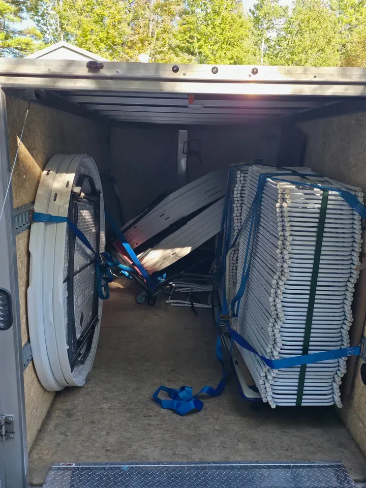 Enclosed trailer with e-track railing and ratchet straps holding rental equipment to the walls. The image shows a failed strap with 10 round tables on a dolly that had fallen over during the drive.