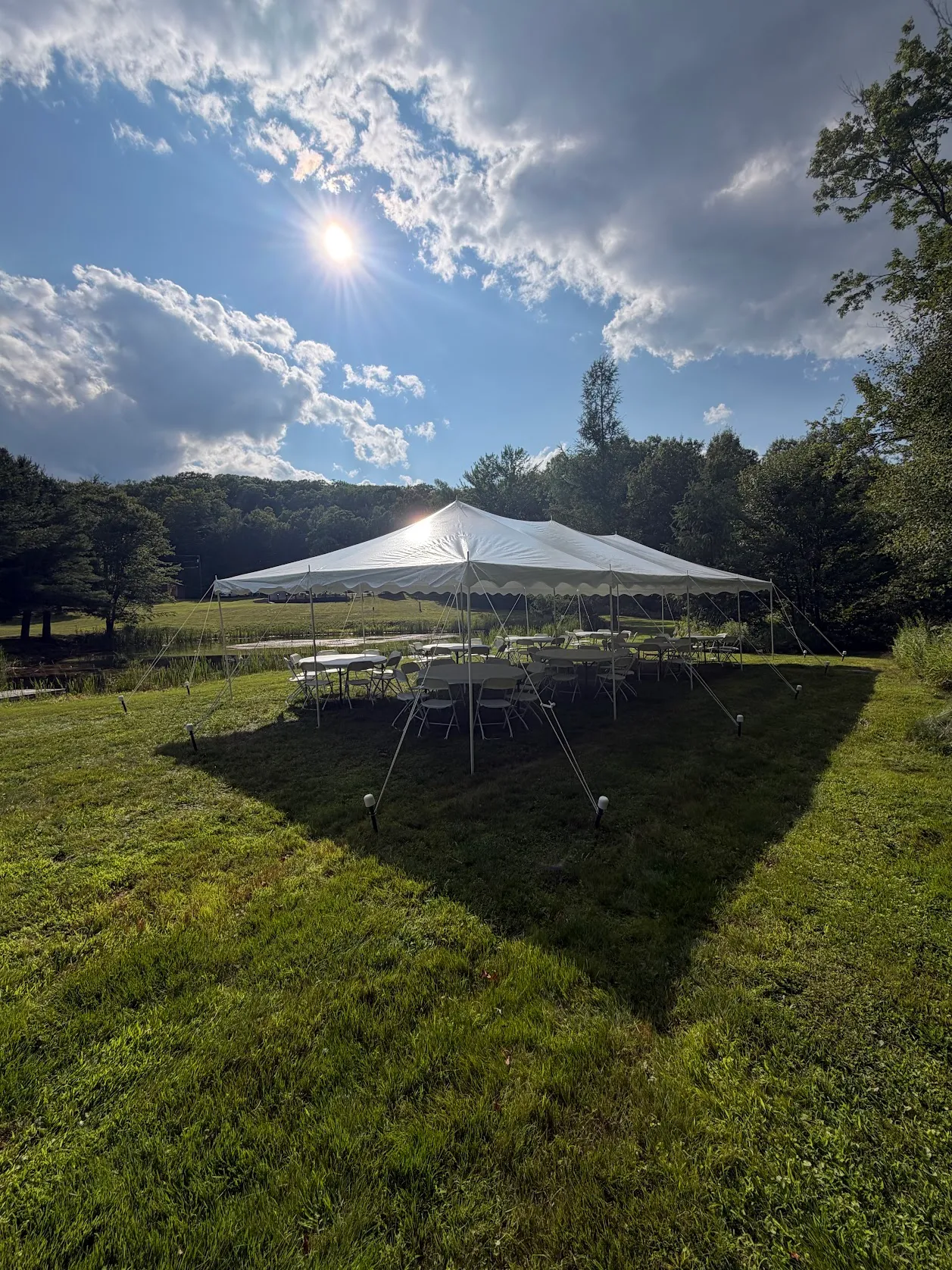 20x40 pole tent setup by a pond with tables and chairs