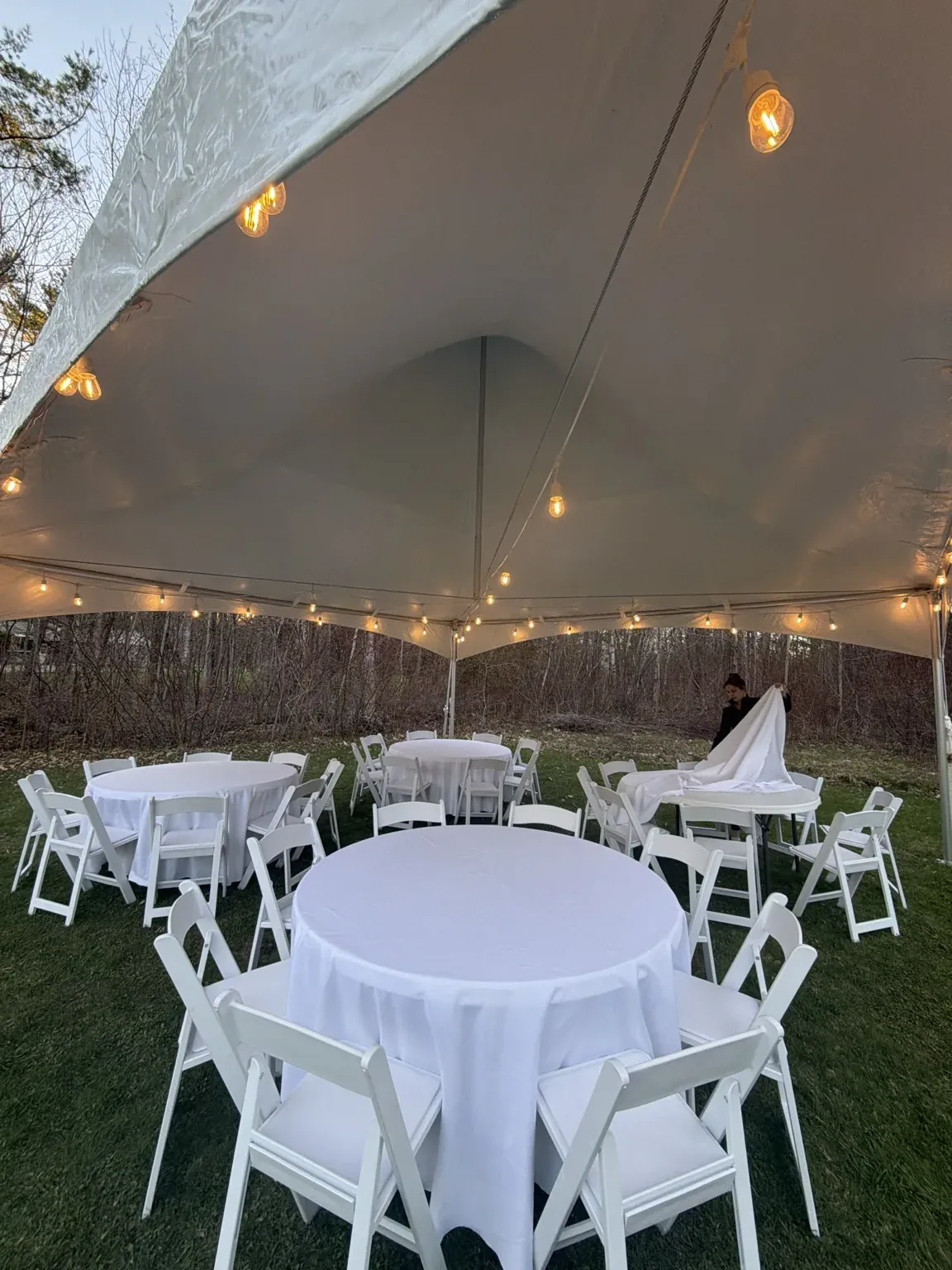 Tables and chairs setup under a tent with Becca the owner of Event Rent Maine putting on linens.