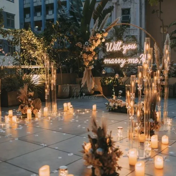 Montaje inspiracional con arco floral de seda, rótulo de neón 'Will You Marry Me?' y iluminación romántica para propuesta de matrimonio.