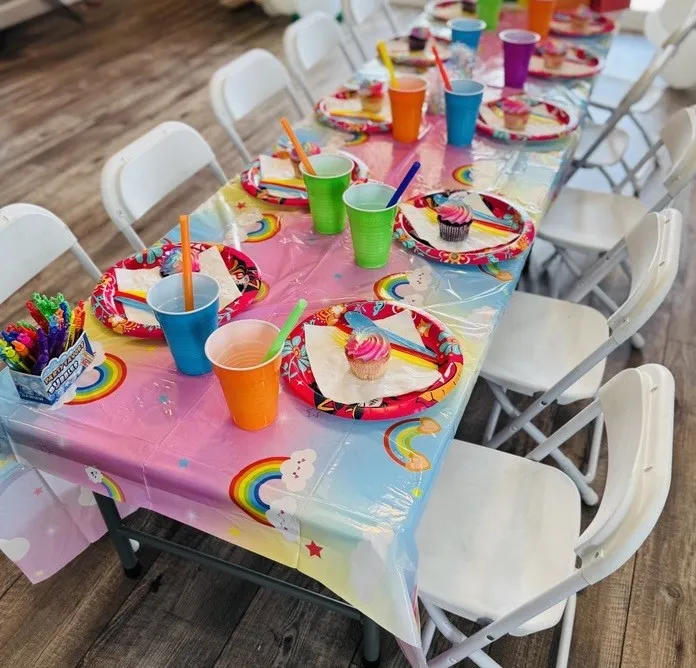Kids’ party setup with white tables and chairs, rainbow decorations, and colorful plates in Denver.