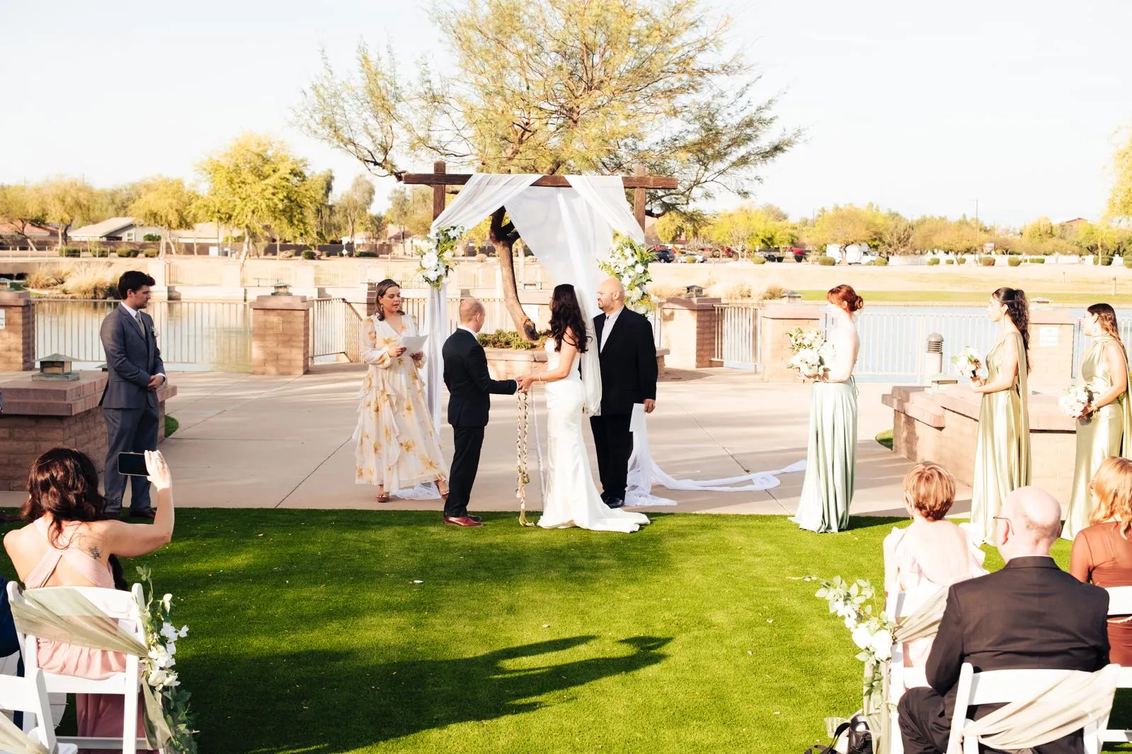 A wedding ceremony with a bride, groom, bridesmaids, groomsmen, officiants, and an arch