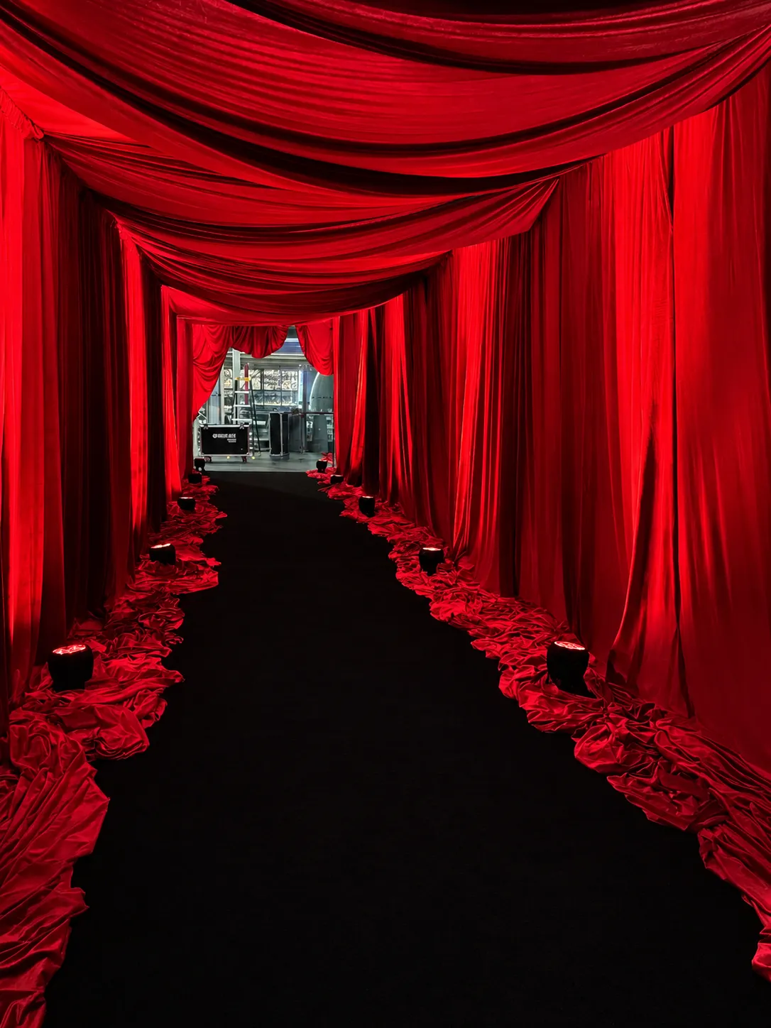 Dramatic red velvet drapery installation 16mts creating an immersive entrance tunnel with layered ceiling swags, floor-to-ceiling curtains and red uplighting.