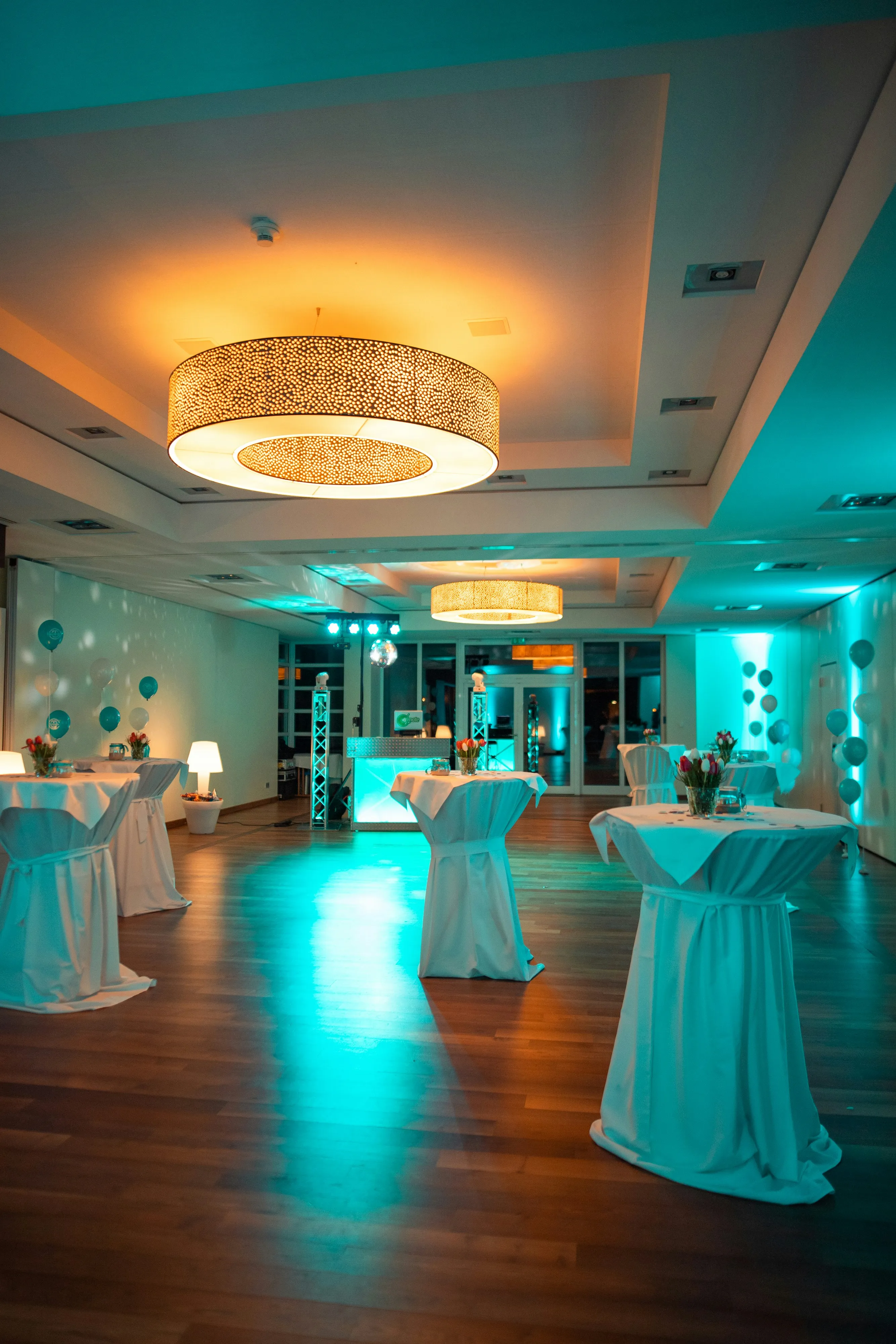 An event venue with tables, balloons, and blue uplighting.