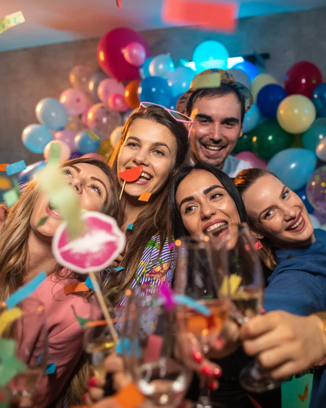 A group of people posing in a photo booth with props and champagne glasses