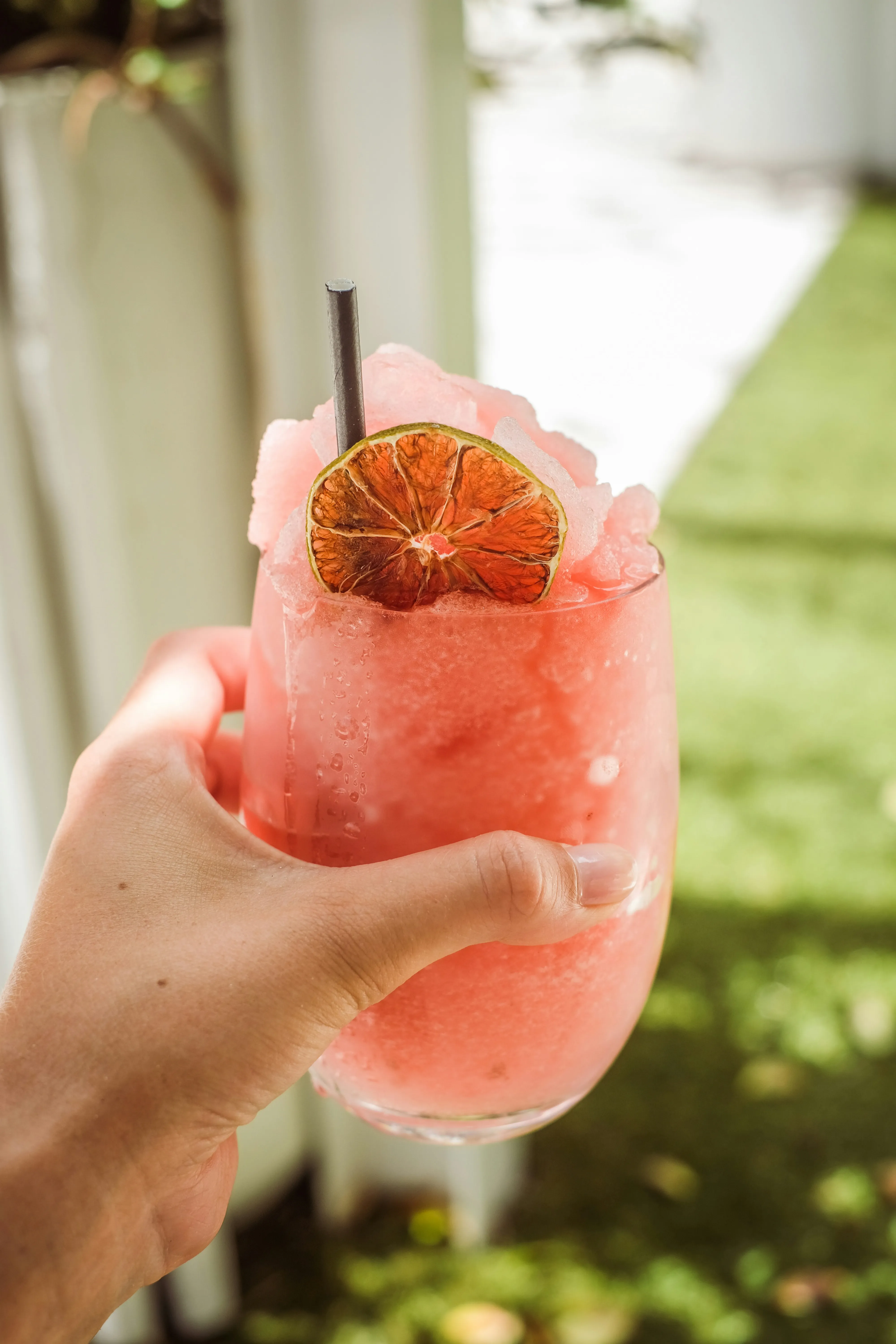 a human hand holding cold glass of pink colored slushie with an out of focus background