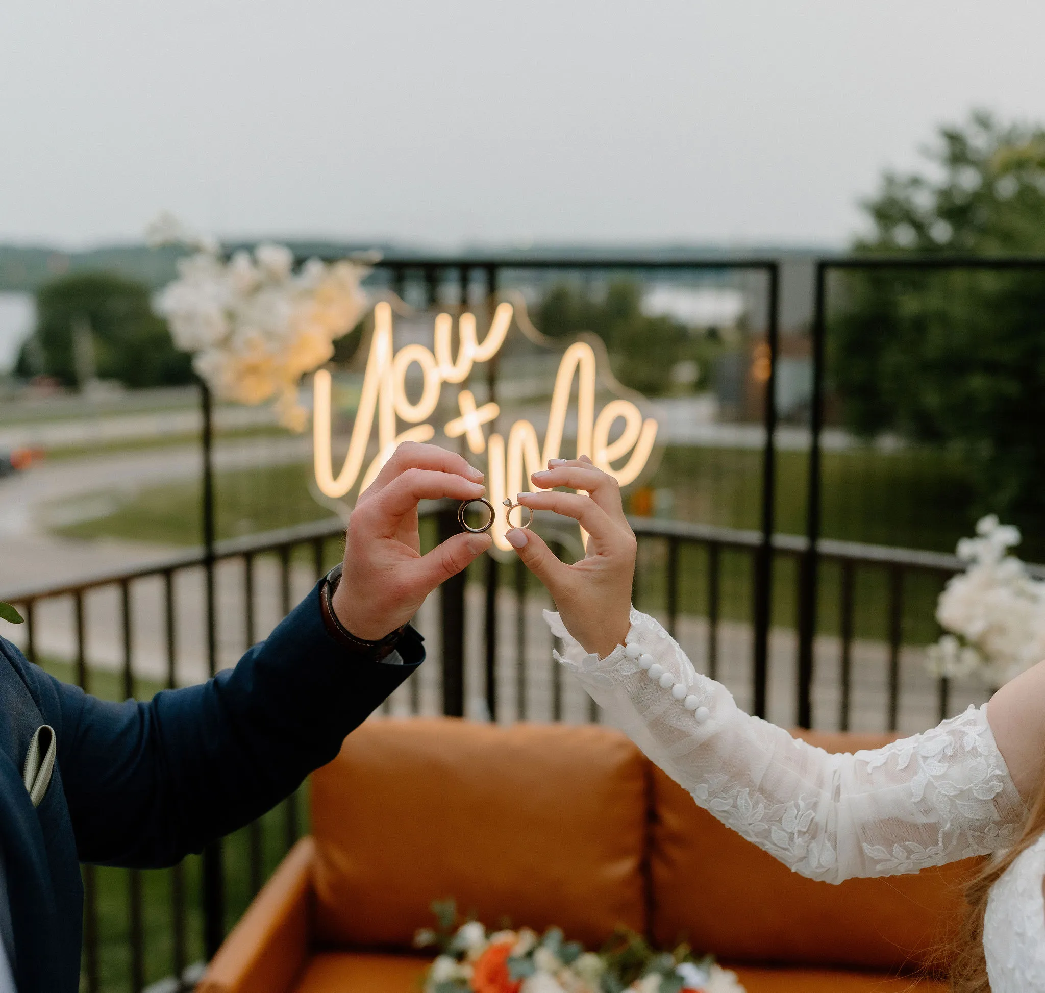 Romantic wedding ring photo in front of neon “You &amp; Me” sign, lounge seating, and modern backdrop by Serenity + Love Event Rentals in Quad Cities Iowa