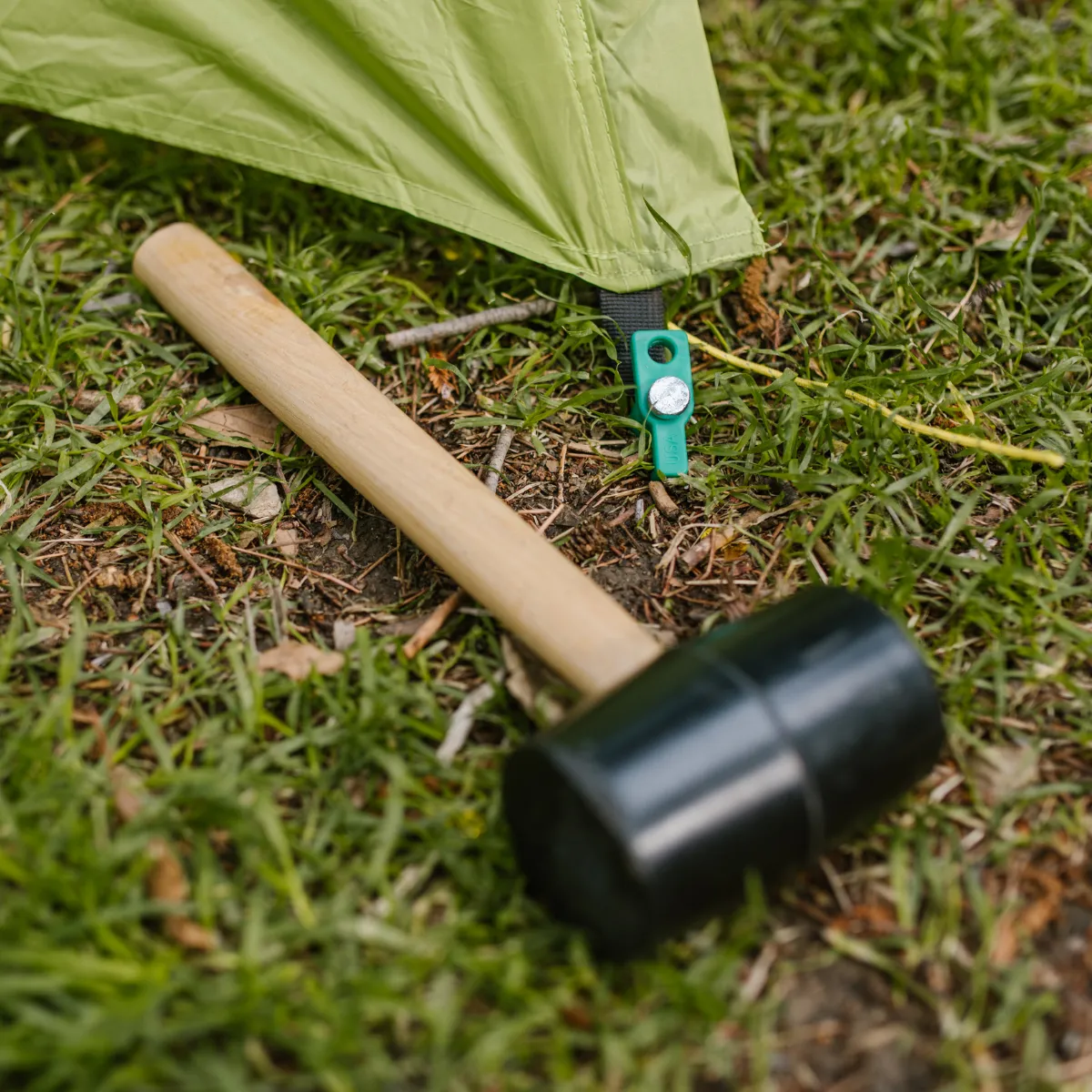 Black rubber mallet and small level lying on the grass beside camping gear.