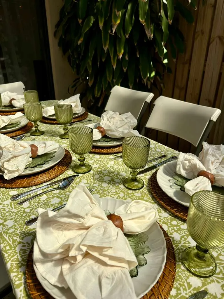 Elegant outdoor dining table with green patterned tablecloth, woven charger, scalloped green plates, and ruffled ivory napkins styled for a spring or summer alfresco tablescape.