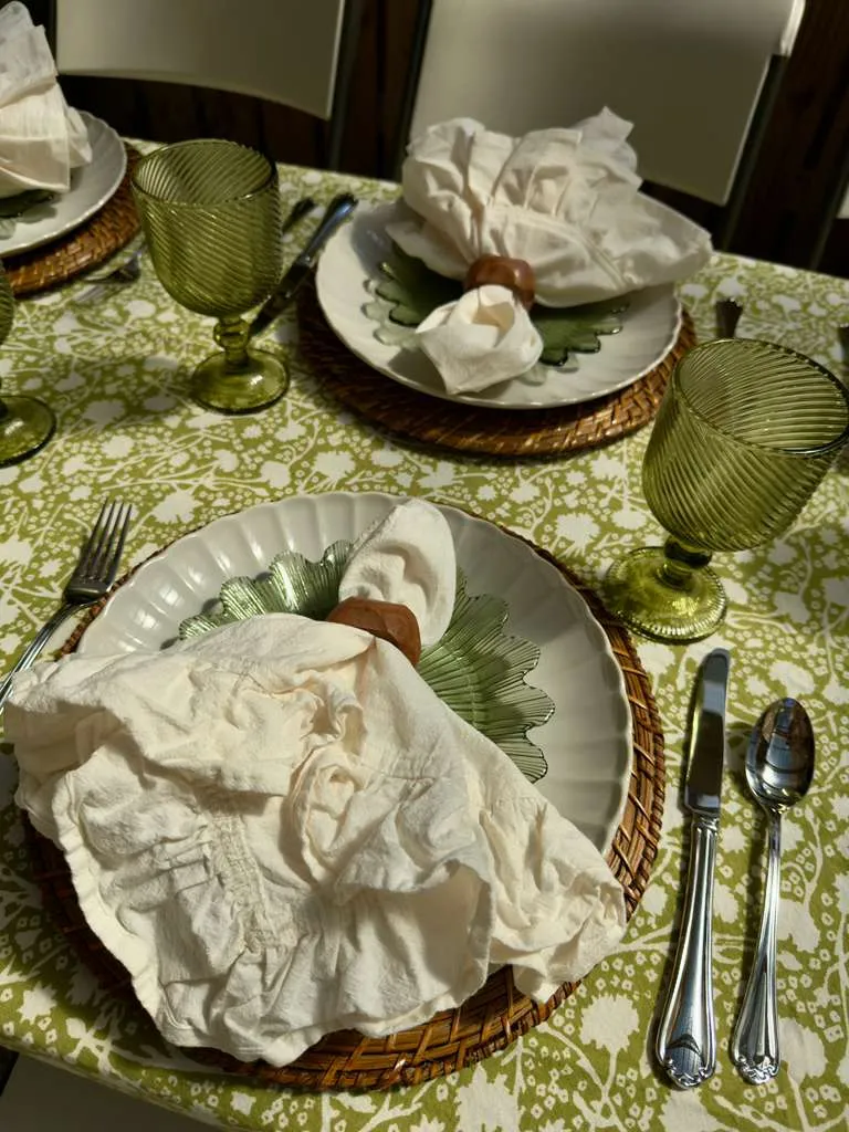 Close up of elegant outdoor dining table with green patterned tablecloth, woven charger, scalloped green plates, and ruffled ivory napkins styled for a spring or summer alfresco tablescape.