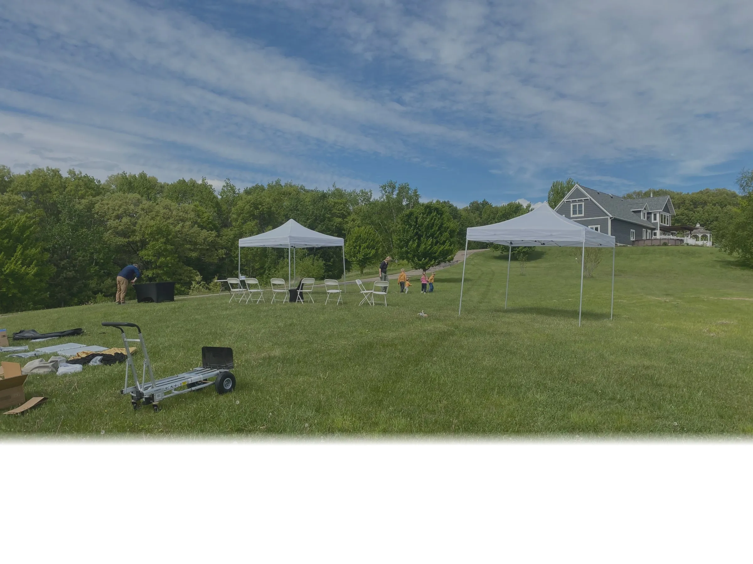 White party tents with tables and chairs set up on a lawn in Eau Claire, WI