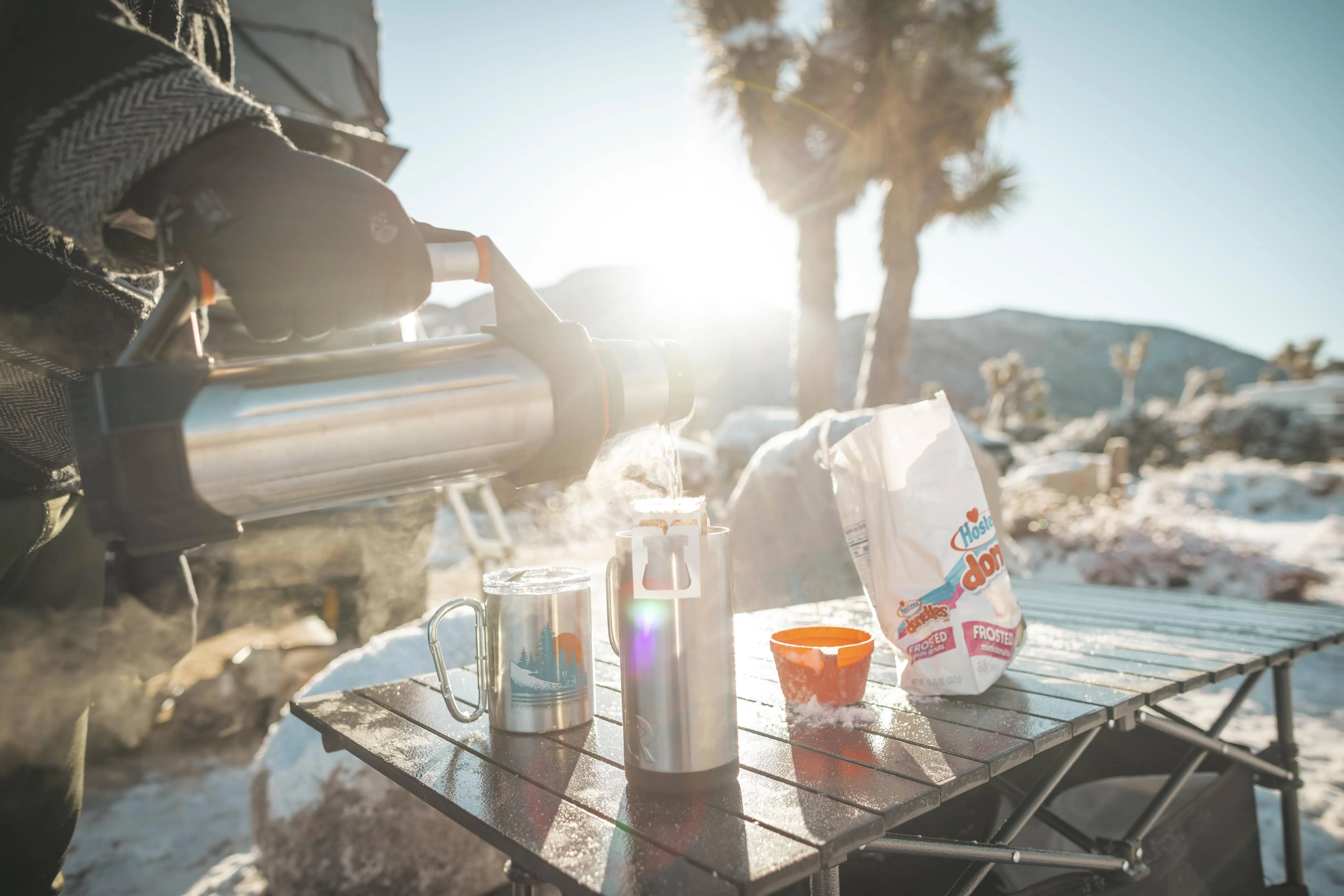 Camper pouring hot water for coffee at a campsite in Joshua Tree with camping gear and a folding table