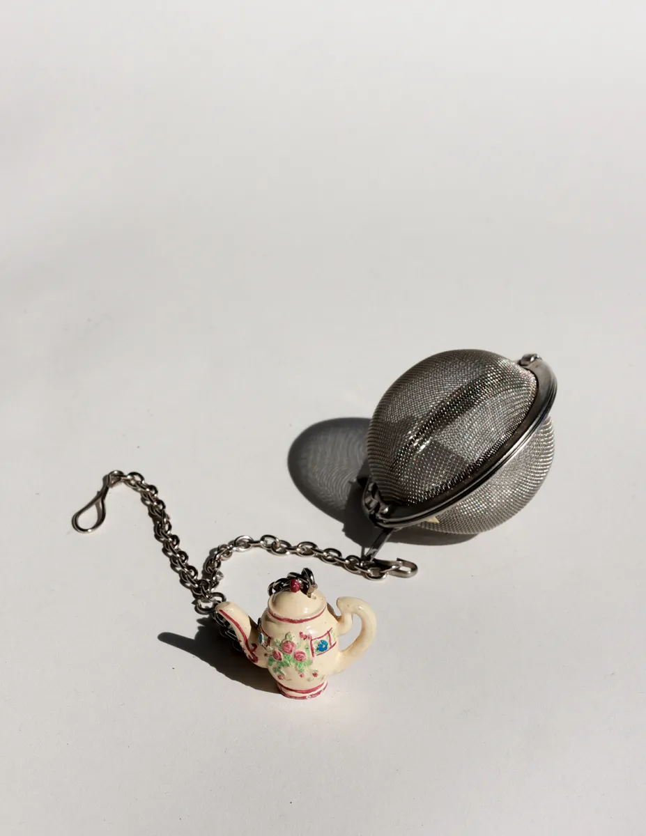 a stainless steel mesh tea infuser with a decorative ceramic teapot charm
