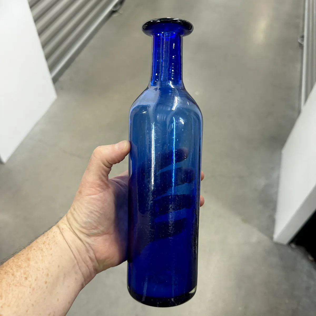 Cylindrical cobalt blue glass bottle is hand made blown glass, with bubbles and flaws, decanter