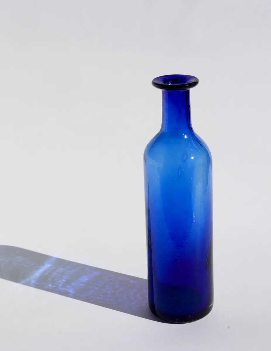 Cylindrical cobalt blue glass bottle is hand made blown glass, with bubbles and flaws, decanter