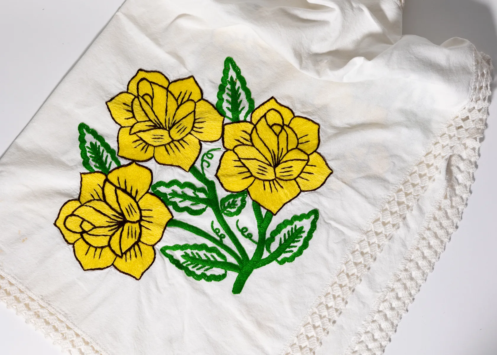White tablecloth with hand embroidered large yellow flowers and green leaves, lacey crocheted edge