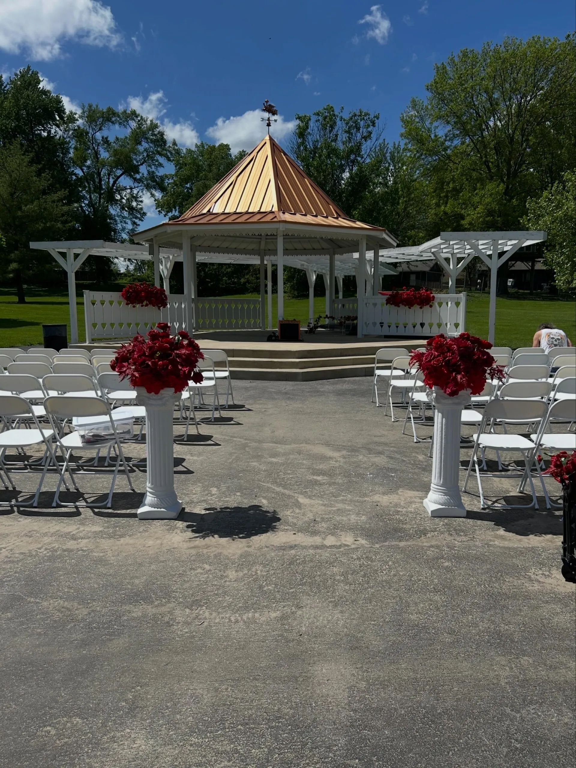 Outdoor wedding ceremony setup with white folding chairs, floral pillars, and gazebo at Rotary Park in Blue Springs Missouri