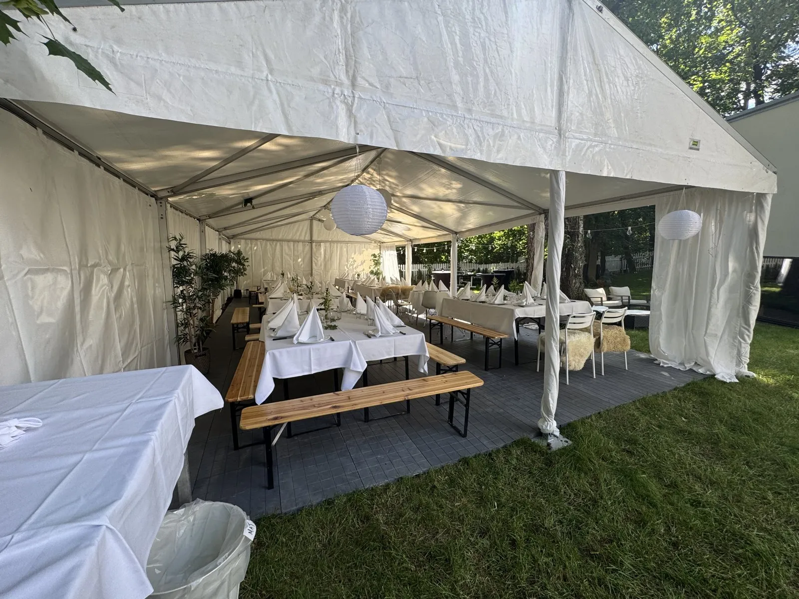 Rammetelt i sommerhagen med dekkede bord, benker og lanterner til firmafest
