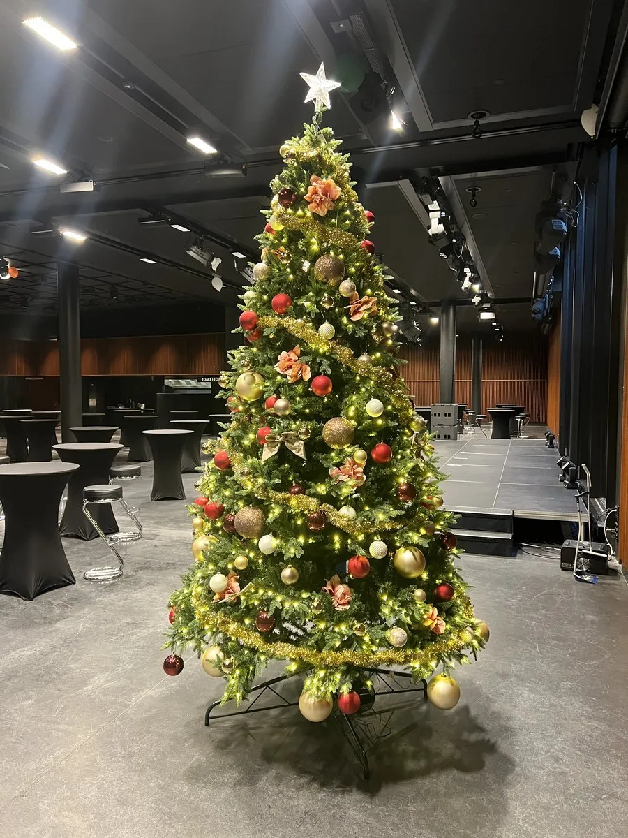 Pyntet juletre med røde og gull kuler i et mørkt selskapslokale
