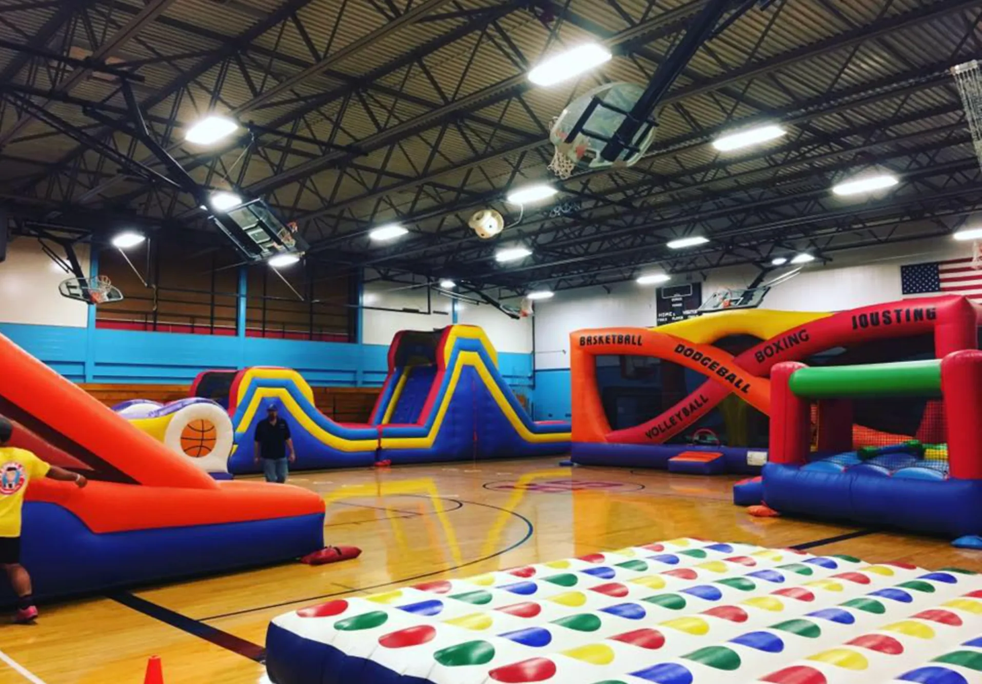 High school students racing through a massive inflatable obstacle course during an outdoor school carnival and post-prom celebration.