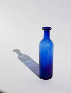 Cylindrical cobalt blue glass bottle is hand made blown glass, with bubbles and flaws, decanter