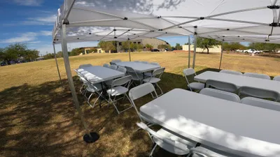 Seating arrangement with 6-ft tables and white folding chairs set under a canopy at park for a birthday party 