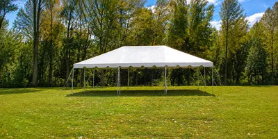 White 20 x 30 frame tent set up on grass with fall trees in the background