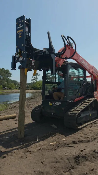 Compact track loader with hydraulic post driver attachment driving vineyard fence posts in Santa Rosa Beach, Florida
