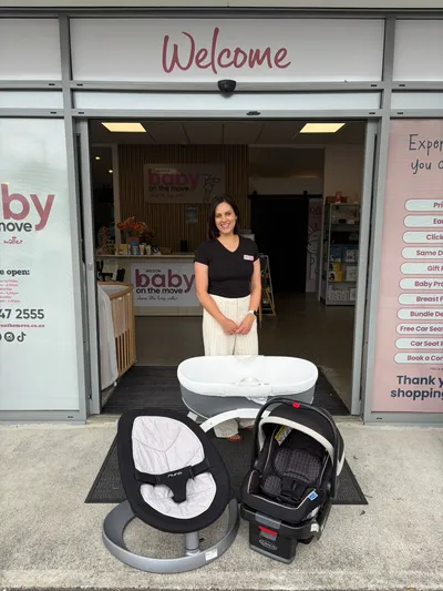 Welcome to Baby On The Move with woman at door of baby shop bassinet, leaf and capsule in front