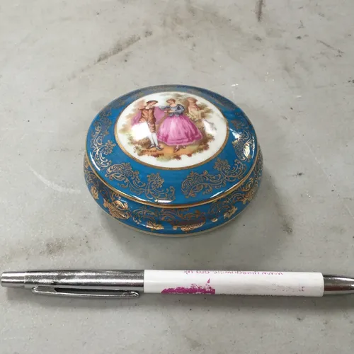 Small blue ceramic trinket pot with gold design edge and image of couple on lid