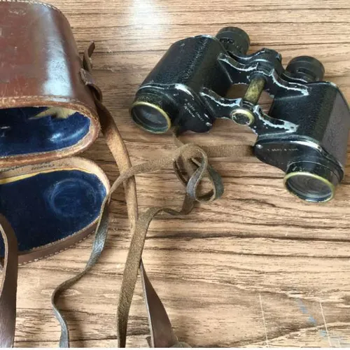 black binoculars its black eye pieces in well-worn brown leather case