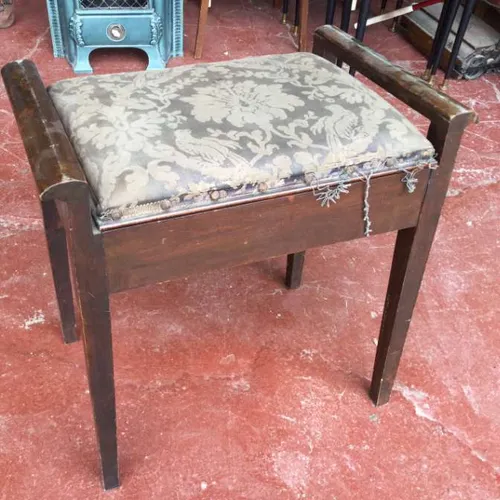 dark wood piano stool with worn floral fabric on hinged seat