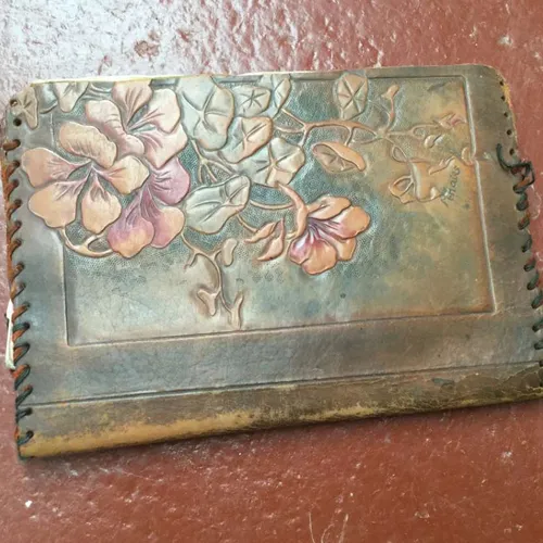 well-worn leather document wallet with floral design and large stitched edging containing scraps of paperwork