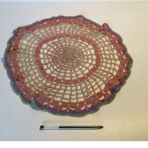 pale pink and beige circular crochet table mat with green and edge