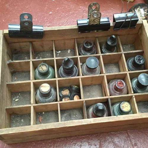 aged tray with 24 compartments containing ink bottles and cork stoppers