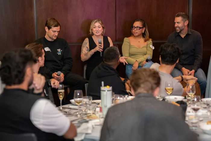 Multiple speakers using microphones during a panel discussion at a corporate event.