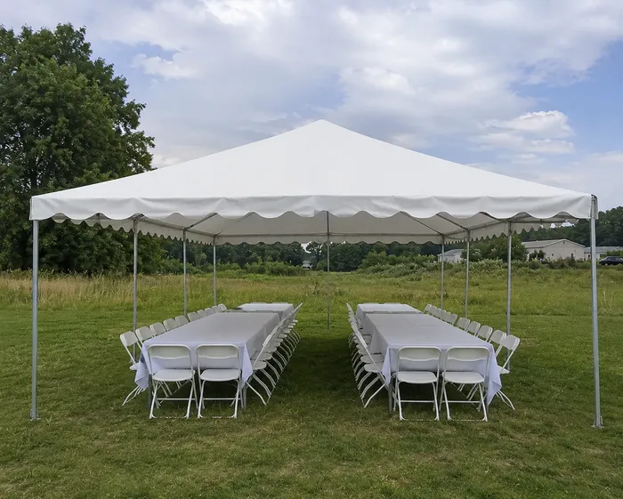 White frame tent with banquet tables and folding chairs set up on grass for a backyard gathering