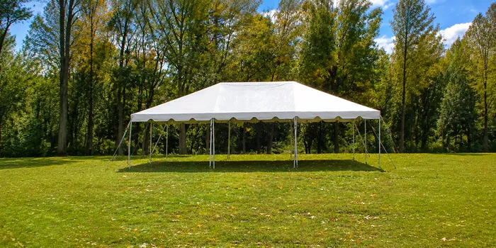 White 20 x 30 frame tent set up on grass with fall trees in the background