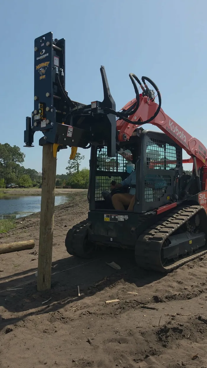 Compact track loader with hydraulic post driver attachment driving vineyard fence posts in Santa Rosa Beach, Florida